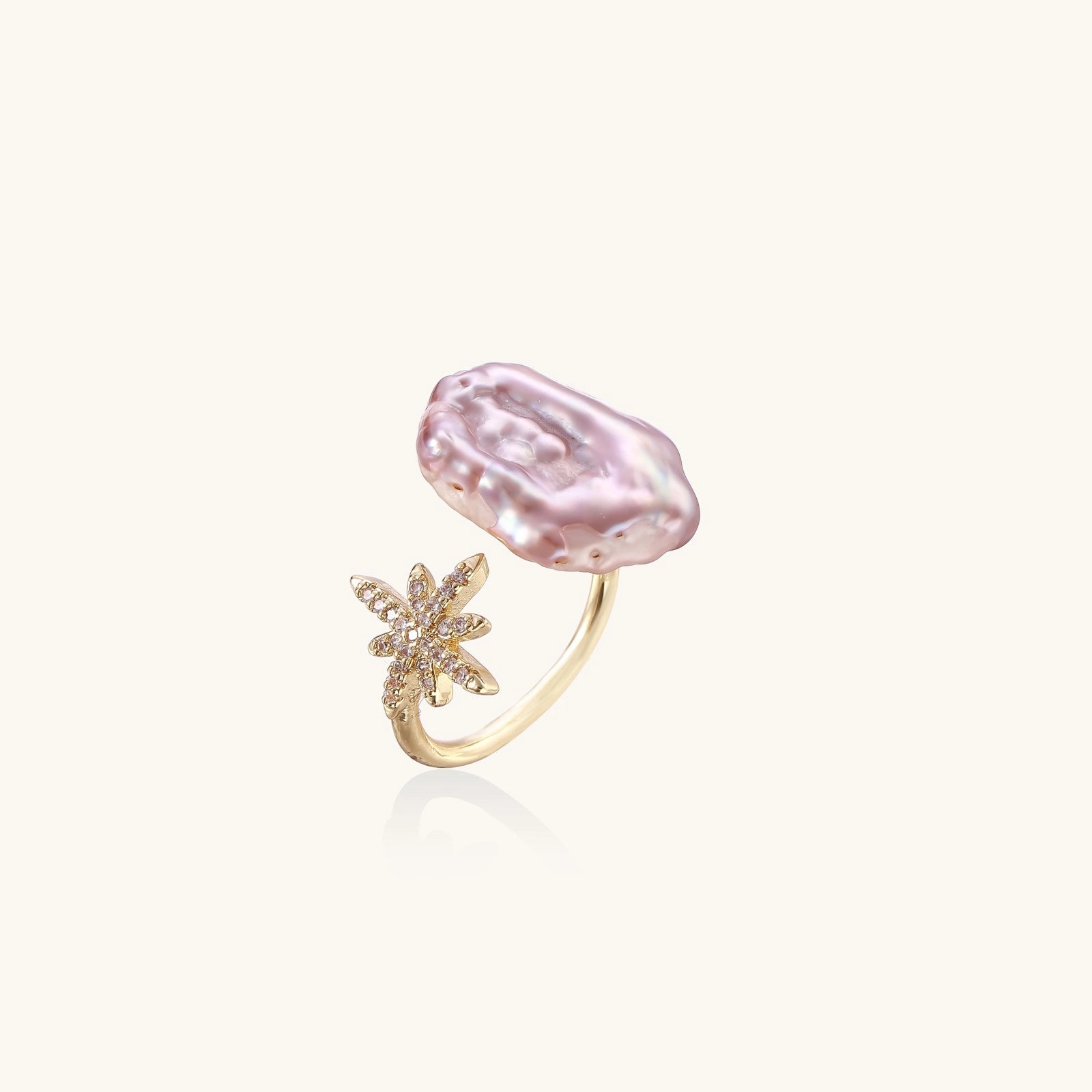Adjustable ring with lavender baroque pearl and crystal star charm on gold-plated band against cream background.