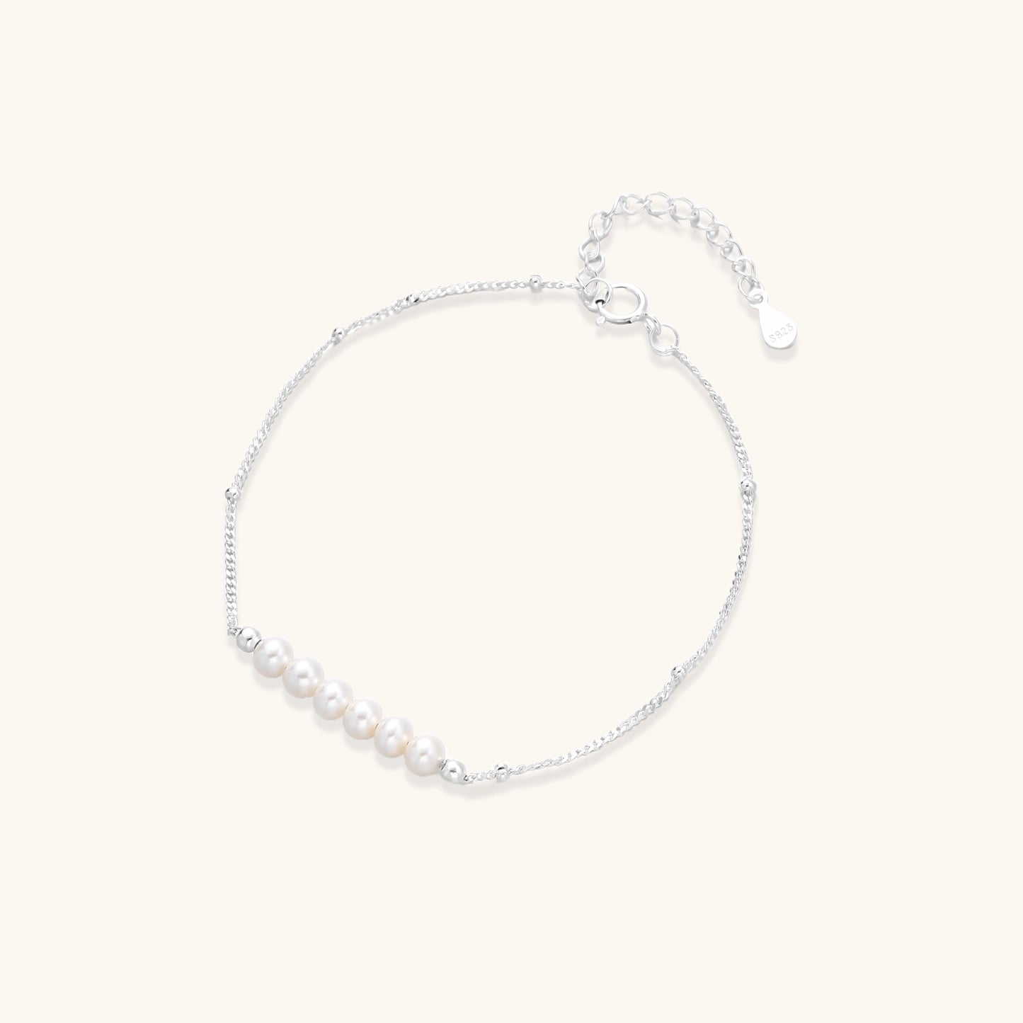 Dainty sterling silver bracelet with small white baroque pearls and adjustable chain on neutral background.