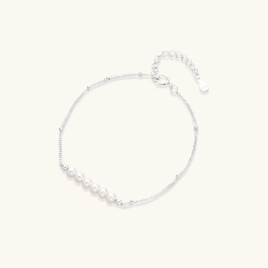 Dainty sterling silver bracelet with small white baroque pearls and adjustable chain on neutral background.