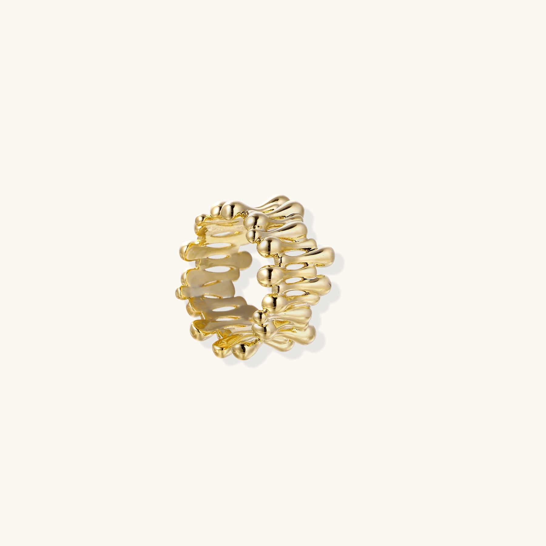Close-up of chunky 18K gold-plated brass ring with flowing wave-like sculptural design on neutral background.