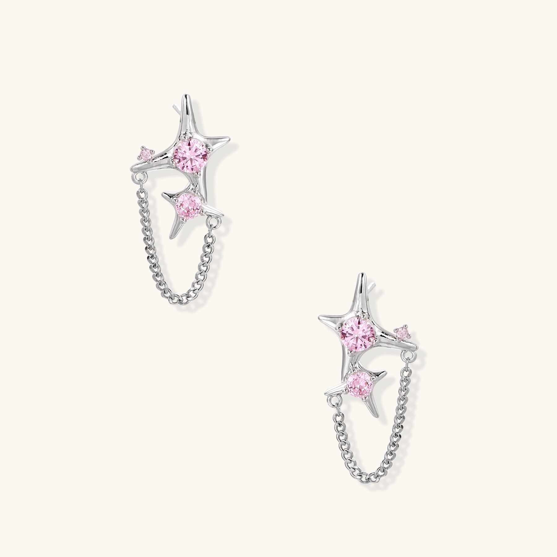 Gold-plated star earrings with pink zirconia stones connected by delicate chains on light background