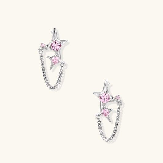 Gold-plated star earrings with pink zirconia stones connected by delicate chains on light background
