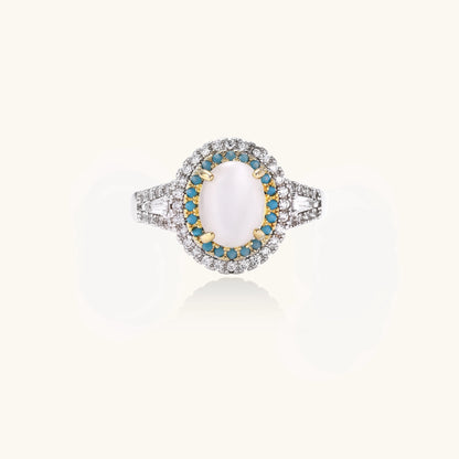 Gold-plated ring with oval cat's eye stone center, blue accent stones, and crystal halo on white background.