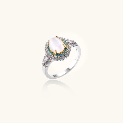 Gold-plated ring with oval cat's eye stone center, blue accent stones, and crystal halo on white background.