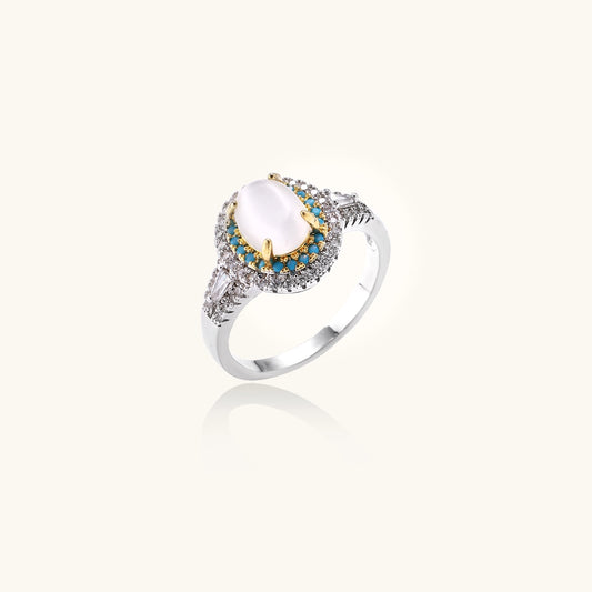 Gold-plated ring with oval cat's eye stone center, blue accent stones, and crystal halo on white background.