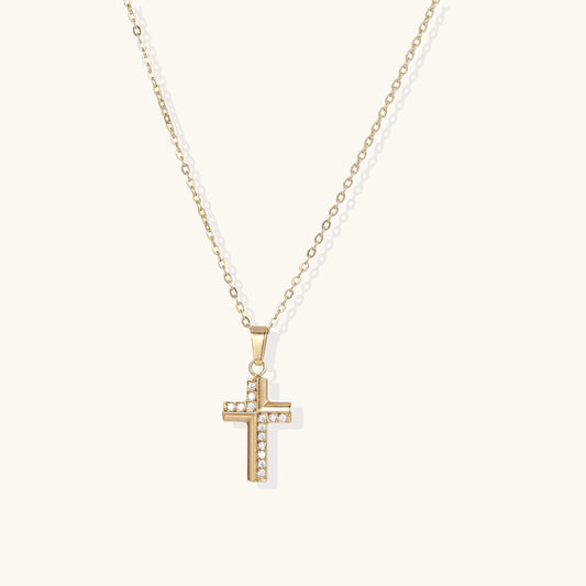 Gold-plated cross pendant necklace with crystal accents on delicate chain against neutral background.