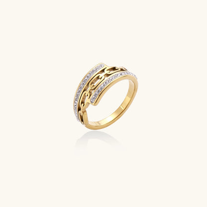 Gold-plated chain-link ring with rhinestone rows on cream background, showing bold geometric design and sparkling details.