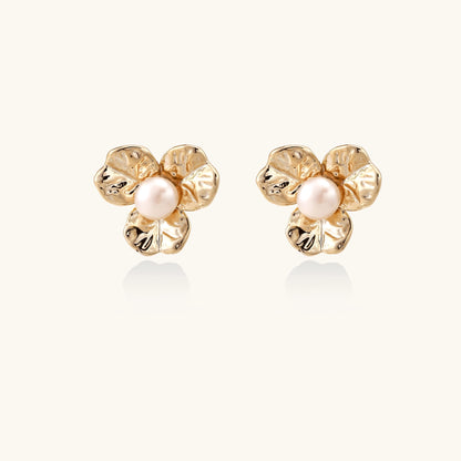 Gold-plated flower stud earrings with freshwater pearl centers on beige background, showing textured petal details.