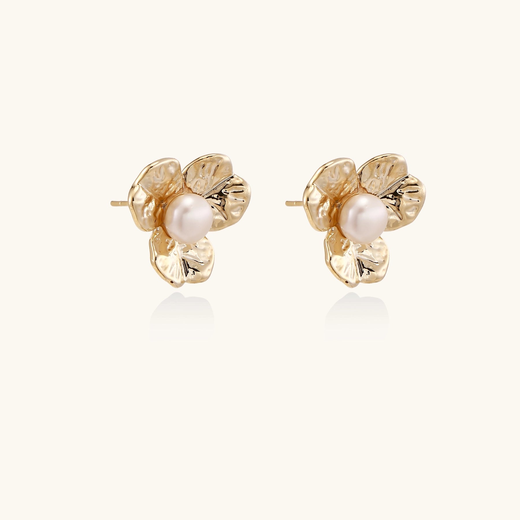 Gold-plated flower stud earrings with freshwater pearl centers on beige background, showing textured petal details.