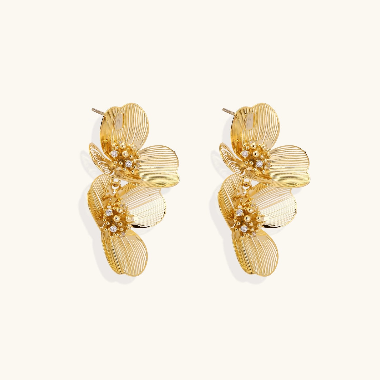 Layered gold-plated floral stud earrings with textured petals and crystal-accented centers on white background.