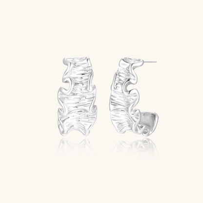 Textured gold-plated hoop earrings with flowing ripple design displayed on clean white background.