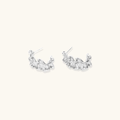 Textured gold-plated hoop earrings with flowing ripple design displayed on clean white background.