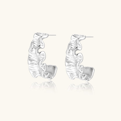 Textured gold-plated hoop earrings with flowing ripple design displayed on clean white background.