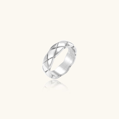 Close-up of a polished stainless steel ring featuring a geometric quilted diamond pattern on white background.