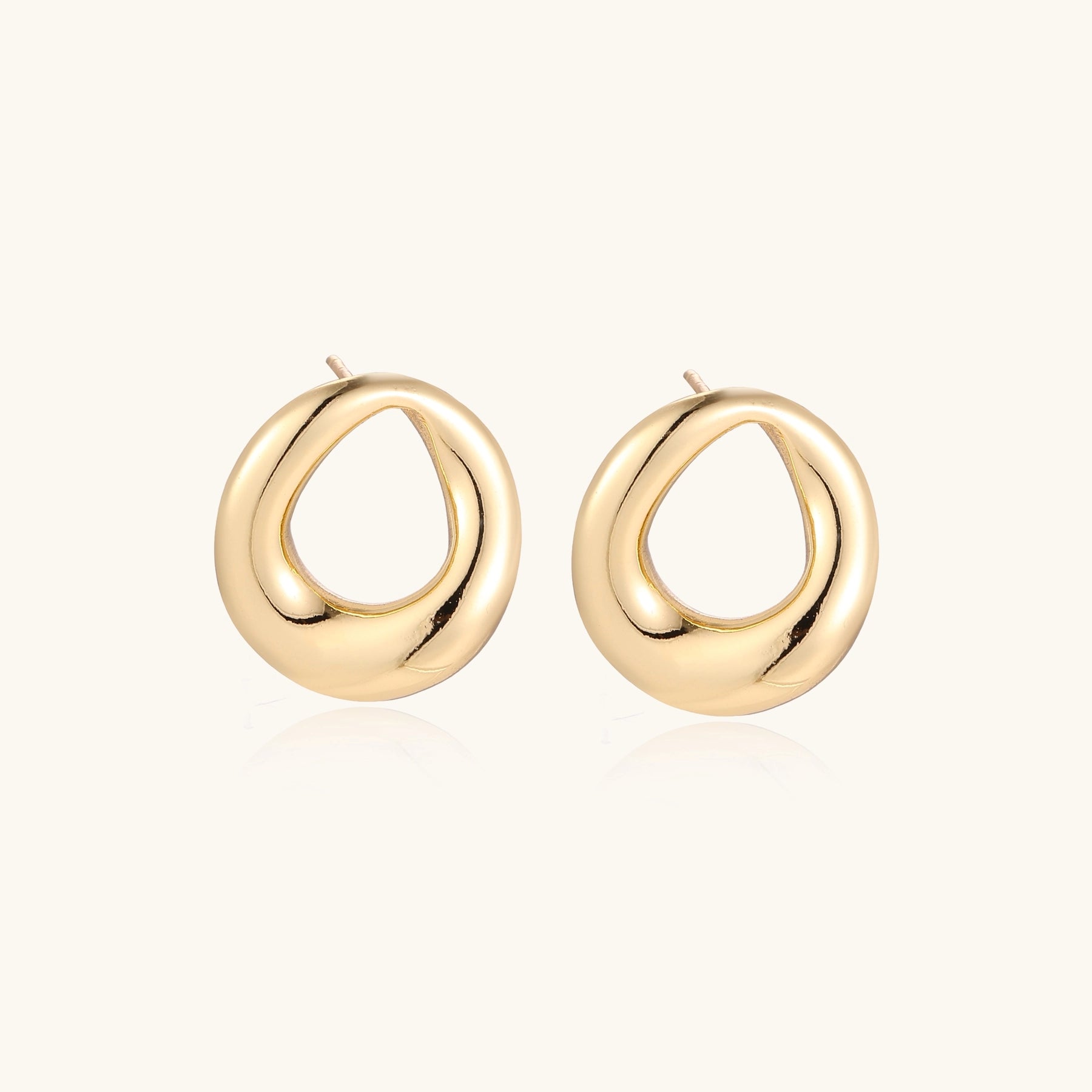 Pair of polished 18K gold-plated stainless steel oval loop stud earrings on cream background