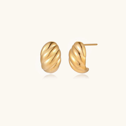 Pair of gold-plated twisted stud earrings with sculptural spiral design displaying elegant curved ridges on cream background.