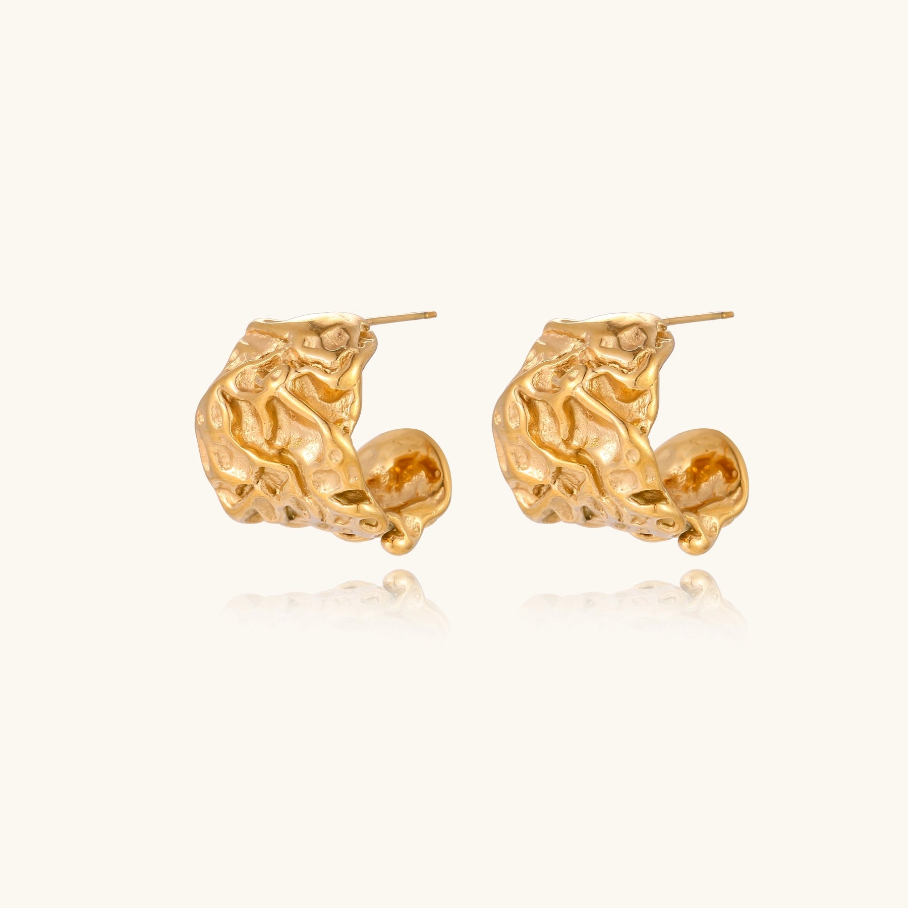 Textured gold-plated hoop earrings with organic molten surface pattern on cream background, showing intricate flowing details.