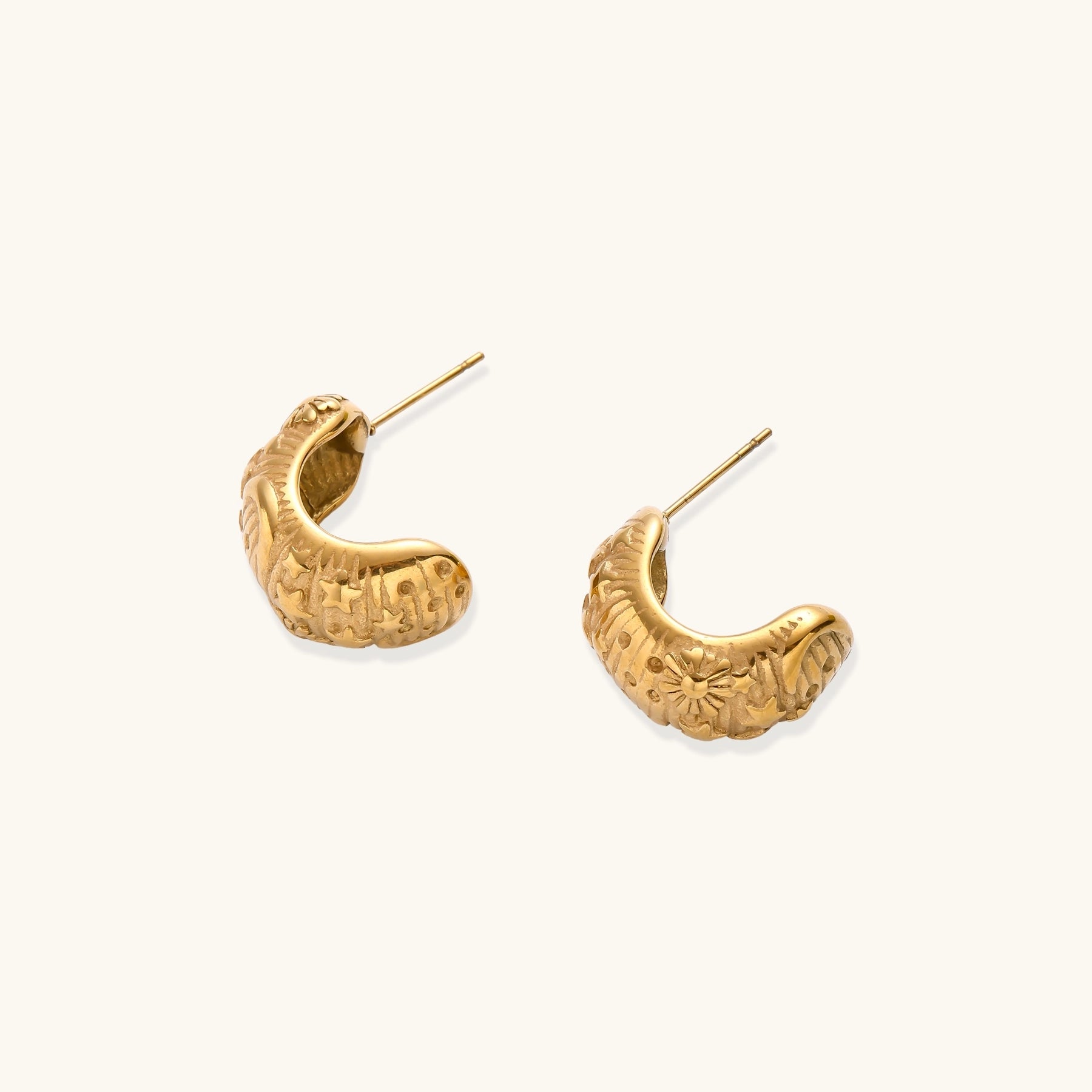 Close-up of ornate 14K gold-plated hoop earrings featuring embossed sun and star celestial motifs on neutral background.