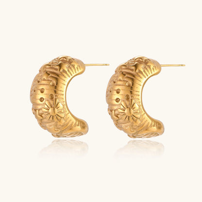 Close-up of ornate 14K gold-plated hoop earrings featuring embossed sun and star celestial motifs on neutral background.